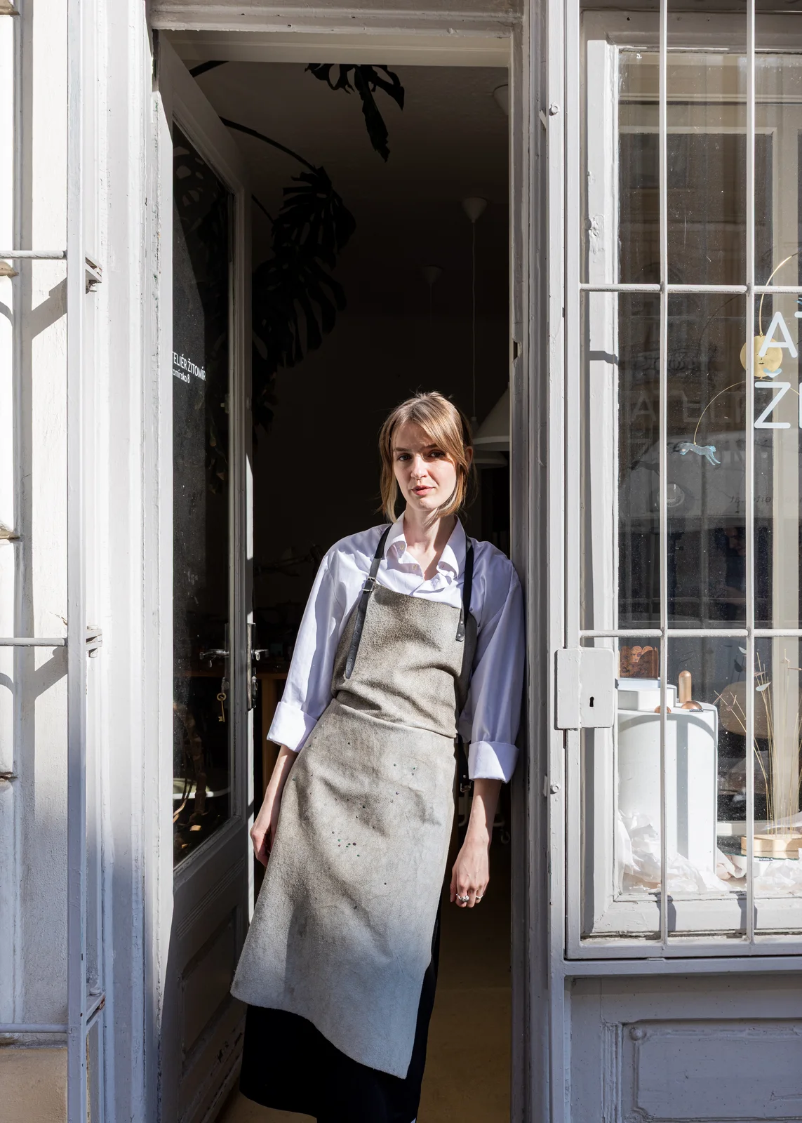 Gabriela Lhotáková stojící v prosklených dveřích svého ateliéru v pracovní zástěře